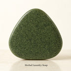 Close-up of one dark botanical-green herbal laundry soap with rounded triangular shape and visible mottled surface texture.
