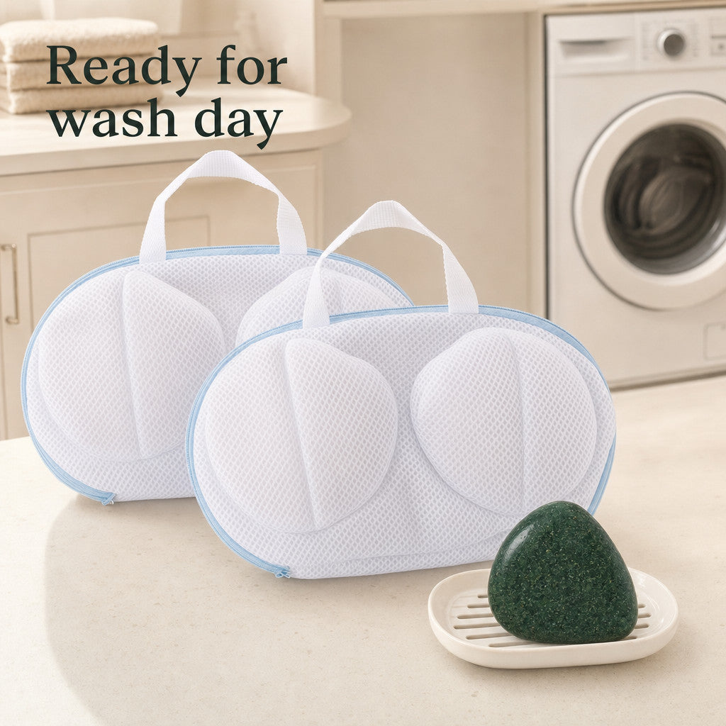 Two original bra wash bags and one green triangular soap on a laundry-room counter with a closed washing machine in the background.