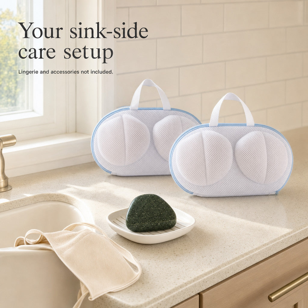 Sink-side intimate-laundry setup with one original green triangular soap and two matching white mesh bra wash bags; lingerie and dish are styling props.